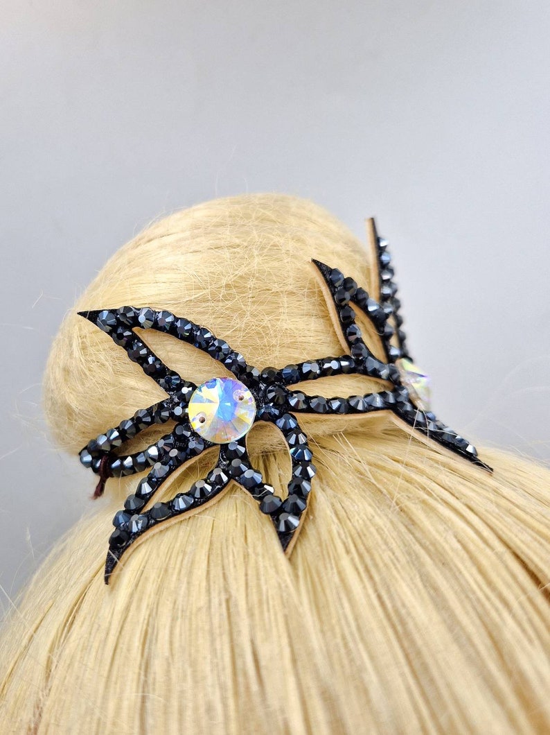 May include: A black hair clip with a large, clear rhinestone in the centre. The clip is shaped like a flower with multiple petals.