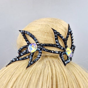 May include: Black hair accessory with two crystal rhinestones. The accessory is shaped like a pair of stylised wings with a black crystal design.
