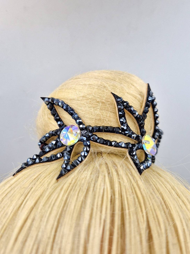 May include: Black hair accessory with two crystal rhinestones. The accessory is shaped like a pair of stylised wings with a black crystal design.