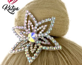 May include: A silver star-shaped hair clip with iridescent rhinestones and a large clear rhinestone in the center. The clip is on a blonde bun.