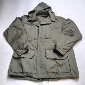 Peut inclure: Une veste à capuche verte avec plusieurs poches et un cordon de serrage au bas.