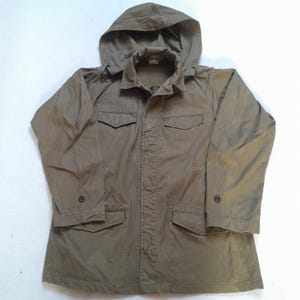 Peut inclure: Une veste de terrain vert olive dotée d'une capuche, d'un col et d'une fermeture à boutons sur le devant. Le vêtement comprend deux poches poitrine à rabat et deux poches inférieures à rabat, ainsi que des manches longues à poignets boutonnés.