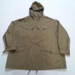 Peut inclure: Une veste à capuche olive de type pullover avec une taille à cordon de serrage, des manches longues à poignets boutonnés et quatre poches avant à rabats boutonnés. Le vêtement présente un col montant avec capuche et un cordon à l'ourlet.