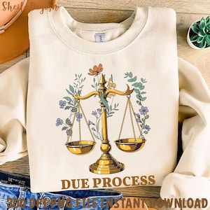 May include: A white sweatshirt with a gold scale design surrounded by colorful flowers. The text "DUE PROCESS" is printed in brown below the scale.