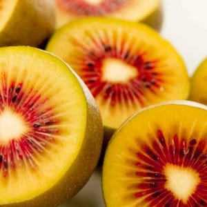 May include: Close-up of several sliced golden kiwis. The kiwis have a vibrant yellow flesh with a striking red center, showcasing a radial pattern of red seeds. The outer skin is a light brown color.