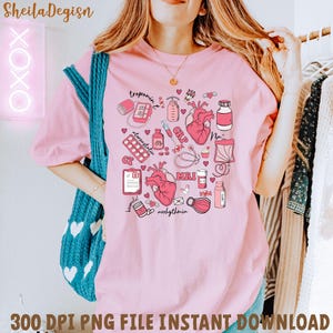 Può includere: Maglietta rosa con un design grafico di illustrazioni mediche relative alla salute del cuore. Il design include un cuore, un elettrocardiogramma, pillole, uno stetoscopio e le parole "troponina", "atorvastatina", "CRP", "MRI" e "aritmia".