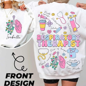 Puede incluir: Sudadera blanca con un diseño colorido en la espalda. El diseño incluye un par de pulmones, un estetoscopio, una taza de café, una mascarilla facial y el texto "RESPIRATORY THERAPIST". La parte delantera de la sudadera tiene un pulmón rosa con flores y el nombre "Isabelle" en texto negro.