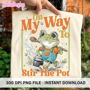 Puede incluir: Camiseta color crema con una rana de dibujos animados con un peto y una cuchara de madera, removiendo una olla. El texto "On My Way To Stir The Pot" se muestra en naranja. También es visible la frase "300 DPI PNG FILE - INSTANT DOWNLOAD".
