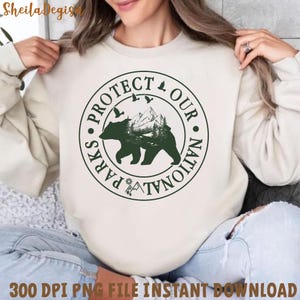 Peut inclure: Un sweat-shirt blanc avec un graphique circulaire vert qui dit "Prot&eacute;gez nos parcs nationaux" avec une silhouette d'ours et de montagne &agrave; l'int&eacute;rieur du cercle.