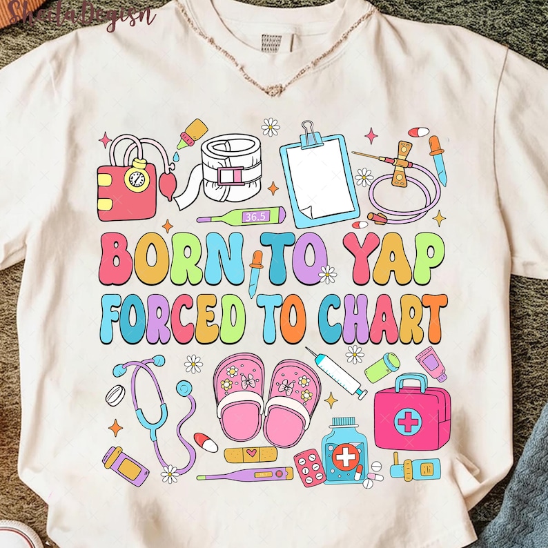 May include: Cream-colored t-shirt with a colorful medical-themed graphic. The design includes medical tools, a blood pressure monitor, and the text "BORN TO YAP FORCED TO CHART" in a playful font. The shirt is decorated with flowers and stars.