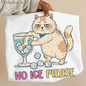 May include: White sweatshirt featuring a grumpy cartoon cat with a blue bow tie, reaching into a glass of water with ice cubes. The text "NO ICE PLEASE" is printed in pink and yellow. The sweatshirt is held by a person.