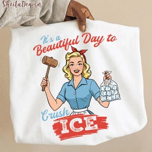 Pode incluir: Saco tote branco com uma ilustração retrô de uma mulher segurando um malho e um saco de cubos de gelo. O texto diz "It's a Beautiful Day to Crush ICE" em letras vermelhas e azuis. O design tem um estilo de quadrinhos vintage.