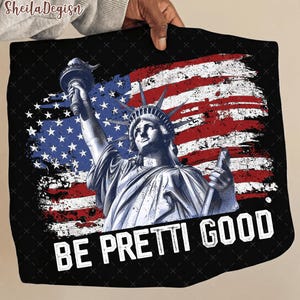 May include: Black square textile featuring a graphic of the Statue of Liberty with an American flag background. The text "BE PRETTI GOOD" is displayed in white. The design is patriotic and artistic.