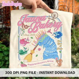 May include: Cream-colored t-shirt featuring a whimsical design with the text "Fauna Bakery" in pink, along with illustrations of birds, fairies, a cake, and a squirrel. The design includes the text "Baked with Love & Magic" and "Once Upon A Dream".