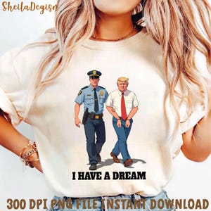 Puede incluir: Una camiseta blanca con un gráfico de un policía y un hombre esposado. El texto "I HAVE A DREAM" está impreso debajo del gráfico.