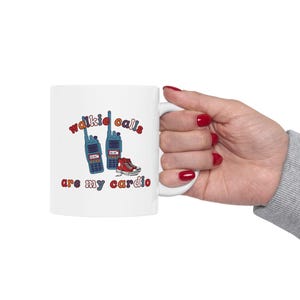 May include: White ceramic mug with the text "walkie calls are my cardio" in red and blue. The mug features illustrations of two blue walkie-talkies and a pair of red sneakers.