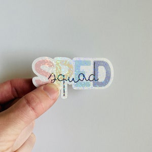 Pu&ograve; includere: Un adesivo olografico con la parola "SPED" in colori arcobaleno e la parola "squad" scritta in corsivo sotto.