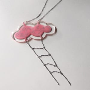 May include: A pink cloud pendant necklace with a silver chain. The cloud is made of clear resin with a pink interior and silver glitter. The chain is attached to the cloud with a series of silver rings.