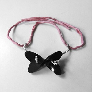 May include: A black butterfly-shaped pendant necklace with a silver twisted wire chain and a pink silk ribbon.