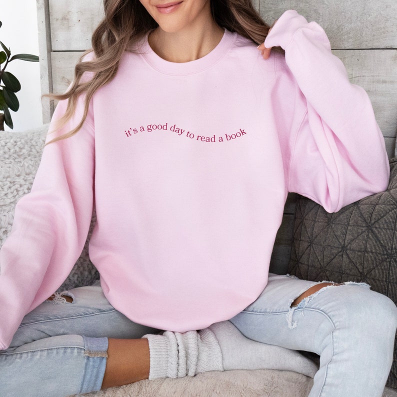 May include: A pink sweatshirt with the text "it's a good day to read a book" in a pink cursive font.