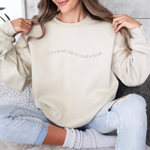 May include: A beige sweatshirt with the text "it's a good day to read a book" printed on the front.