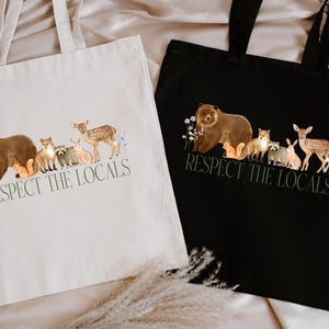May include: Two tote bags with the text "Respect the Locals" printed on them. The bags are made of canvas and have a black and white design. The design features a bear, deer, fox, raccoon, squirrel, and rabbit.