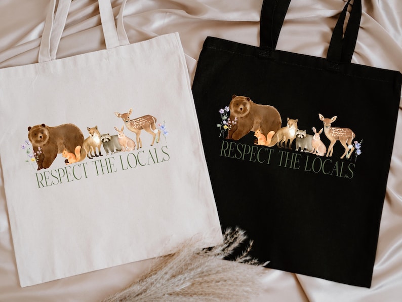 May include: Two tote bags with the text "Respect the Locals" printed on them. The bags are made of canvas and have a black and white design. The design features a bear, deer, fox, raccoon, squirrel, and rabbit.