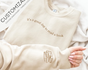 May include: A beige sweatshirt with the text "it's a good day to read a book" embroidered on the front and a stack of books embroidered on the sleeve.