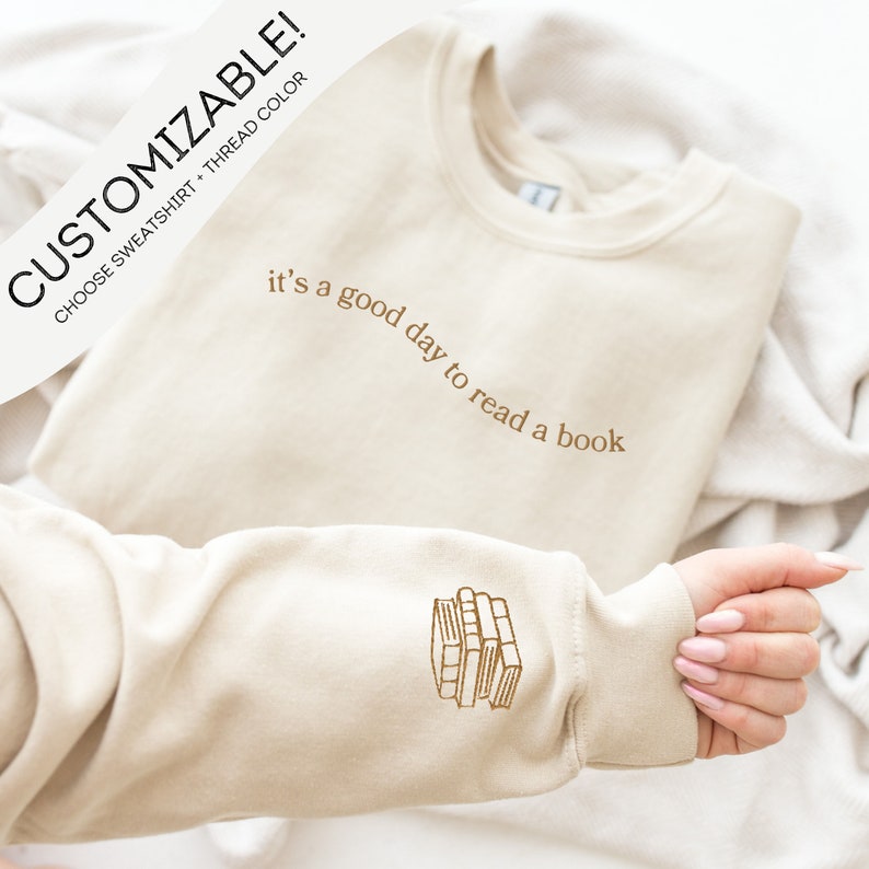 May include: A beige sweatshirt with the text "it's a good day to read a book" embroidered on the front and a stack of books embroidered on the sleeve.