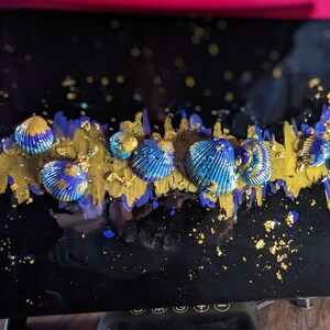 May include: A black resin art piece with a gold and purple abstract design. The piece is decorated with blue and gold seashells.