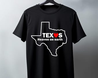 May include: Black t-shirt featuring a white outline of the state of Texas with the word "TEXAS" and a red heart. Below the word is the phrase "Heaven on earth". The t-shirt is hanging on a black hanger.