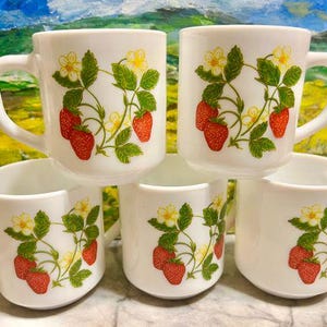 May include: Set of five white ceramic mugs with a strawberry design. Each mug features a cluster of red strawberries, green leaves, and small yellow flowers. The mugs have a classic handle design and are suitable for hot or cold beverages.