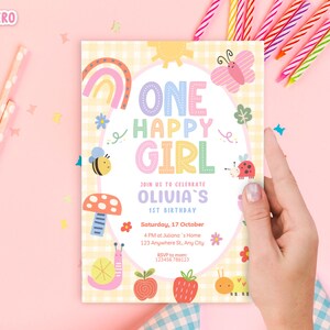 May include: A pastel-colored birthday invitation with the text "ONE HAPPY GIRL" and "OLIVIA'S 1ST BIRTHDAY". The design includes a rainbow, butterfly, bee, mushroom, ladybug, snail, apple, strawberry, and caterpillar. The invitation is held by a hand.
