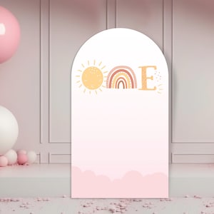 Puede incluir: Un telón de fondo de arco rosa y blanco con un sol, un arcoíris y la letra "E" en estilo boho. El telón de fondo es perfecto para una fiesta de primer cumpleaños.