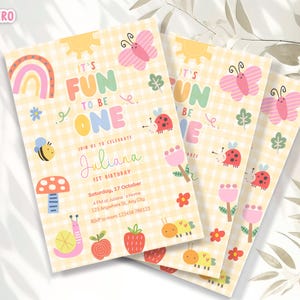 May include: A stack of colorful birthday invitations with a yellow gingham background. The invitations feature illustrations of a rainbow, sun, butterfly, bee, and other cute graphics. Text on the invitation reads "It's Fun to be One" and includes the name "Juliana".