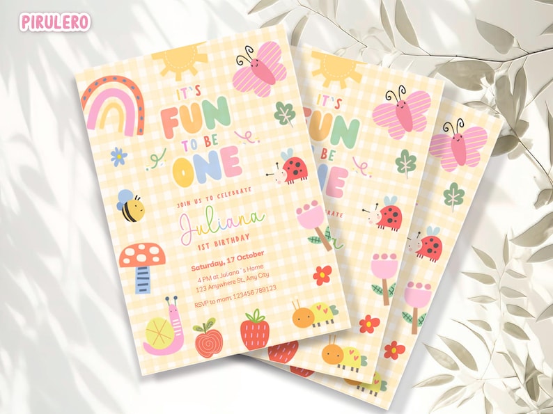 May include: A stack of colorful birthday invitations with a yellow gingham background. The invitations feature illustrations of a rainbow, sun, butterfly, bee, and other cute graphics. Text on the invitation reads "It's Fun to be One" and includes the name "Juliana".
