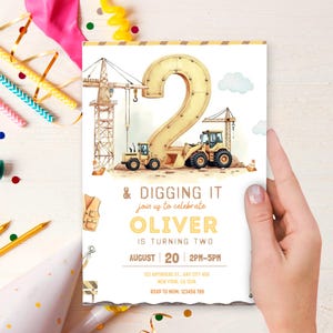 May include: A birthday invitation featuring a watercolor illustration of construction vehicles and a large number 2. The text reads "& Digging It" and "Oliver is turning two". The invitation is held by a hand.