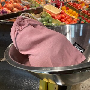 May include: A pink reusable produce bag with the text "green essentials" printed on it. The bag is sitting in a stainless steel bowl.
