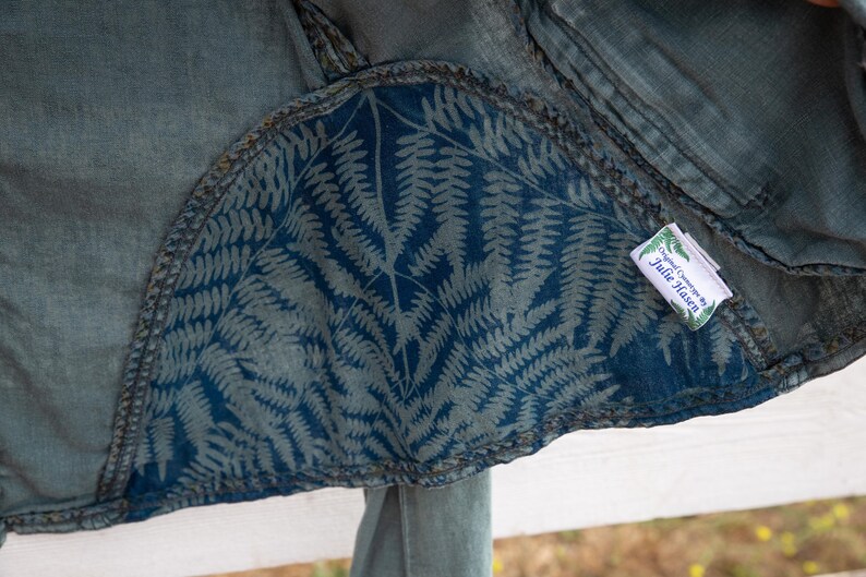 Puede incluir: Una chaqueta vaquera azul con un forro de estampado de helechos y una etiqueta blanca que dice "Designed & Crafted by Julie Hasen".