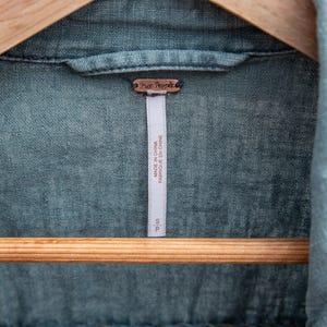 Puede incluir: Una camisa vaquera azul con una etiqueta de Free People. La etiqueta dice "Made in China" y "Fabriqu&eacute; en Chine".