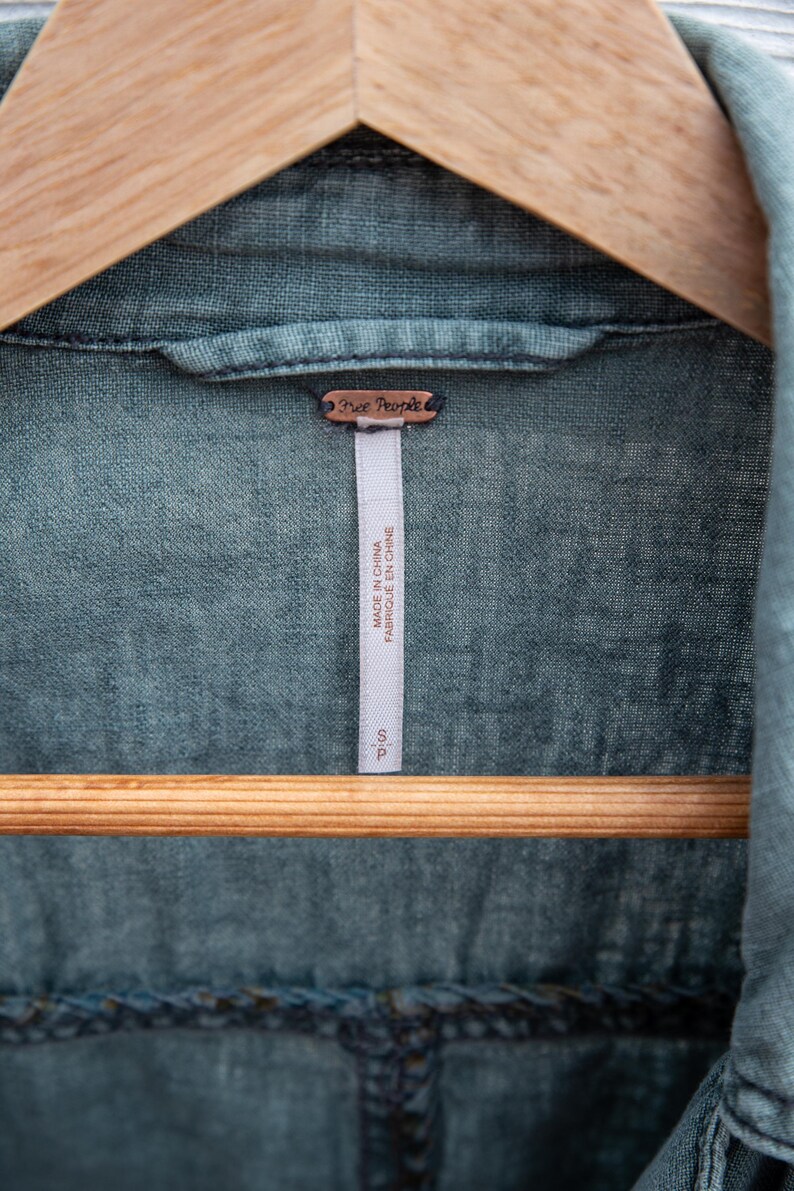 Puede incluir: Una camisa vaquera azul con una etiqueta de Free People. La etiqueta dice "Made in China" y "Fabriqu&eacute; en Chine".