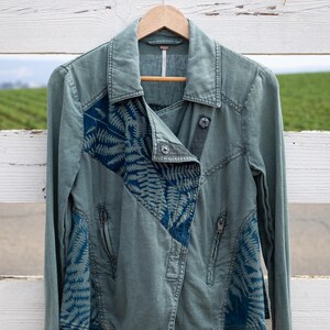 Puede incluir: Una chaqueta vaquera verde con un estampado de helechos azules en las mangas y el frente. La chaqueta tiene cierre de cremallera y cuello.