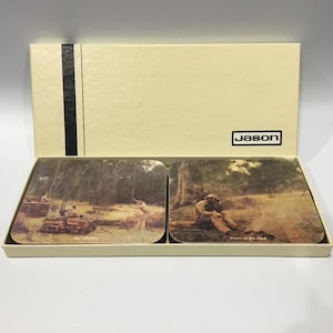 May include: A set of two rectangular coasters with landscape paintings, in a cream box with a black stripe and the brand name "Jason". The coasters feature forest scenes with figures. The box is designed to hold the coasters securely.