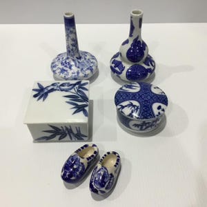 May include: A collection of white and blue porcelain items including two vases, a square lidded box with bamboo motifs, a round lidded container with geometric patterns, and a pair of miniature clogs decorated with windmill illustrations.