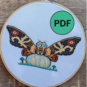 May include: A cross-stitch pattern in a wooden embroidery hoop featuring a moth with large blue eyes, orange and black wings with red circular accents, perched on a textured egg, with a green circle containing the text PDF in the corner.