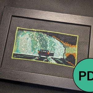 May include: Cross-stitch artwork of a waterfall and vehicle, framed in a dark grey wooden frame. The artwork is displayed within a black mount. A green circle with the word "PDF" is in the lower right corner.