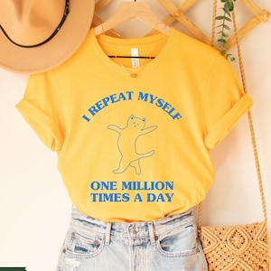 May include: Yellow t-shirt with a blue cat graphic and the text "I repeat myself one million times a day".