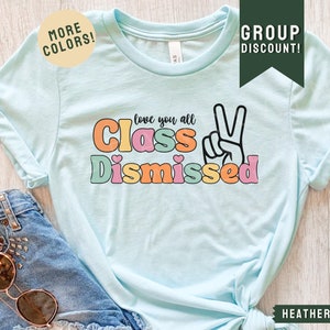 May include: A light blue t-shirt with the text "love you all Class Dismissed" in colorful letters with a peace sign. The text is in a retro font style.