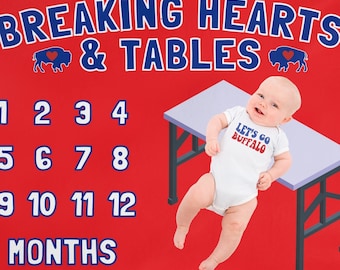 Puede incluir: Manta roja para hitos de bebé con un logotipo de búfalo azul y el texto "Breaking Hearts & Tables". La manta tiene una mesa blanca con un bebé encima que lleva un body blanco con el texto "Let's Go Buffalo". La manta también tiene los números del 1 al 12 para cada mes.