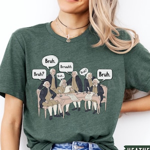 May include: A green t-shirt with a graphic of six men in colonial attire sitting around a table. The men are all wearing powdered wigs and have speech bubbles above their heads that say 'Bruh', 'Bruh?', 'Bruh', 'Bruh', 'Bruh', and 'Bruh.' The text 'HEATHER FOREST' is printed in white at the bottom of the image.